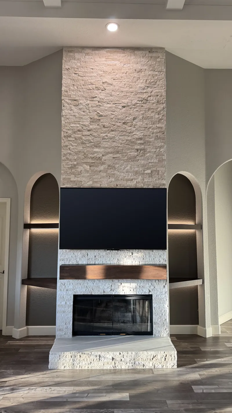 Stacked stone fireplace rising to the ceiling between two arched niches with lit dark shelves